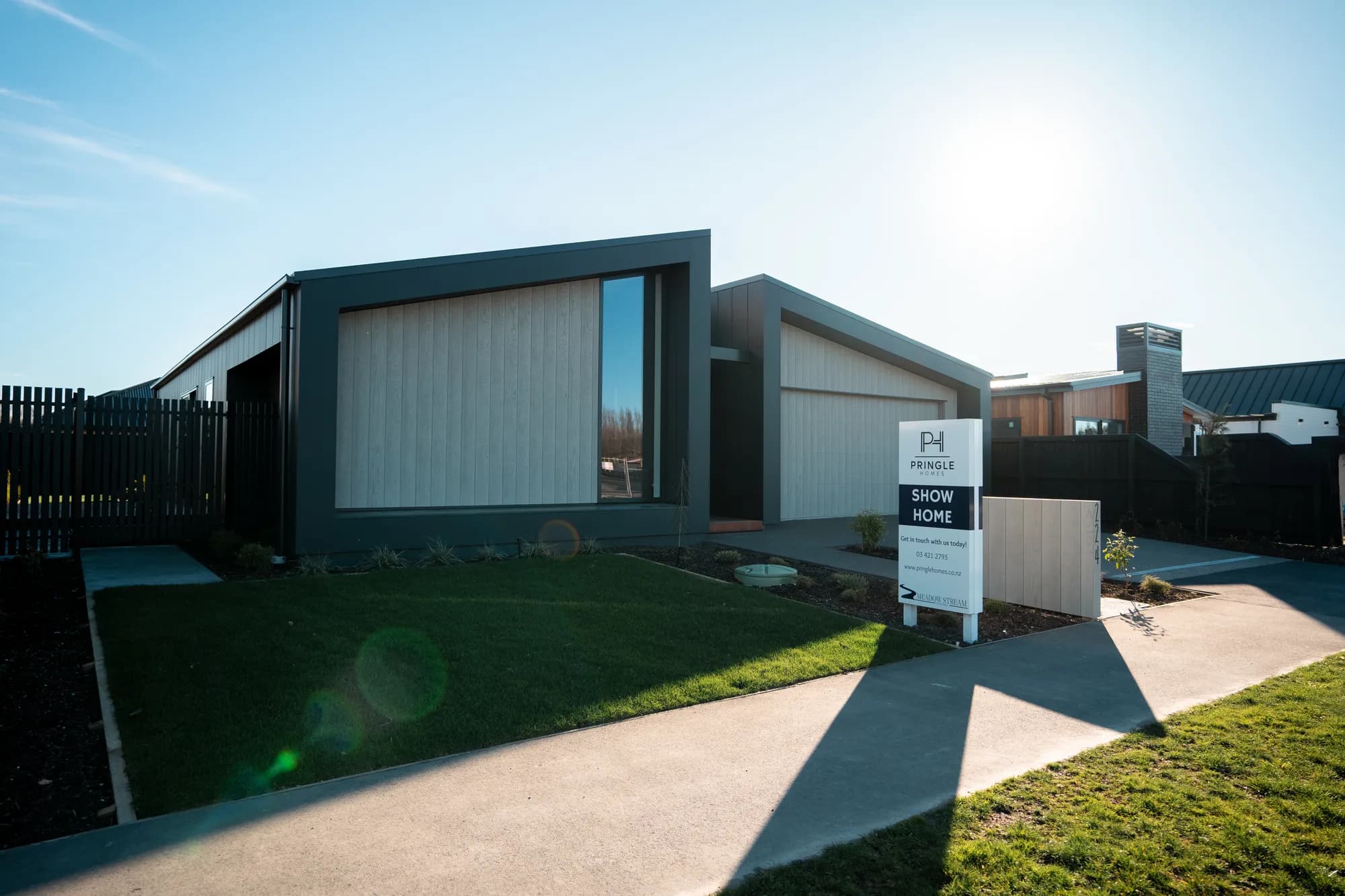 The Meadow Stream show home at Casebrook in low winter sun, pale vertical cladding in a dark frame, with the Pringle Homes show home sign on the front lawn