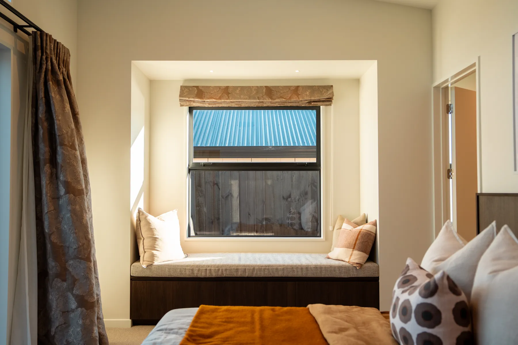 A window seat built into the reveal of a bedroom window at the Meadow Stream show home, with a timber base and a patterned blind